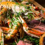 Close-up cooked langoustine at the centre of a surf and turf platter.