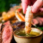 Langoustine tail being dipped in garlic butter as part of a surf and turf dinner.