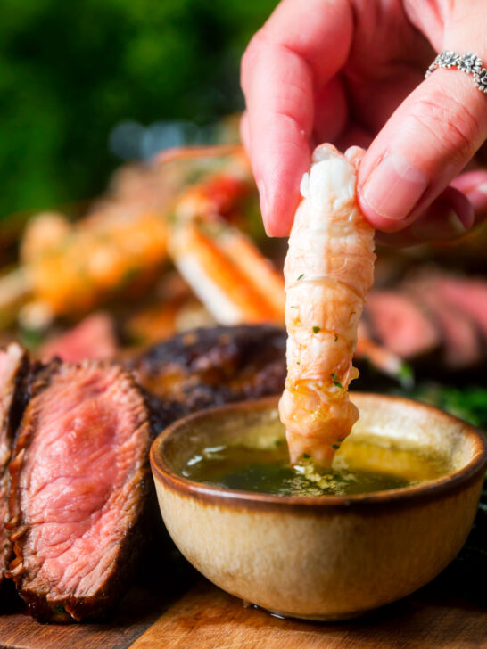 Langoustine tail being dipped in garlic butter as part of a surf and turf dinner.