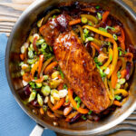 Overhead roasted sweet and sour pork fillet with peppers in a pan.