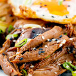 Close-up shredded teriyaki duck leg served as part of a donburi rice dish.