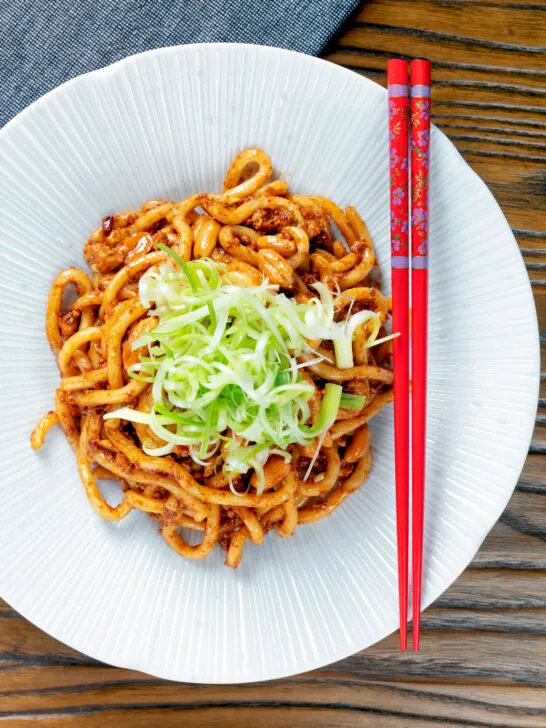 Overhead vegan tofu noodle stir fry with peanuts and dan dan sauce garnished with spring onions.