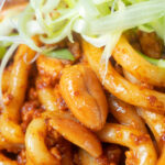 Close-up crumbled tofu noodle stir fry with peanuts and spicy dan dan sauce.