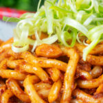 Close-up tofu udon noodle stir fry with peanuts and spicy dan dan sauce.