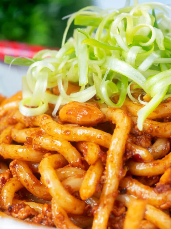 Close-up tofu udon noodle stir fry with peanuts and spicy dan dan sauce.