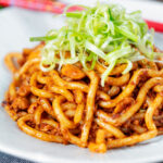 Vegan tofu noodle stir fry with peanuts and dan dan sauce garnished with spring onions.