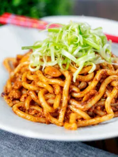 Vegan tofu noodle stir fry with peanuts and dan dan sauce garnished with spring onions.