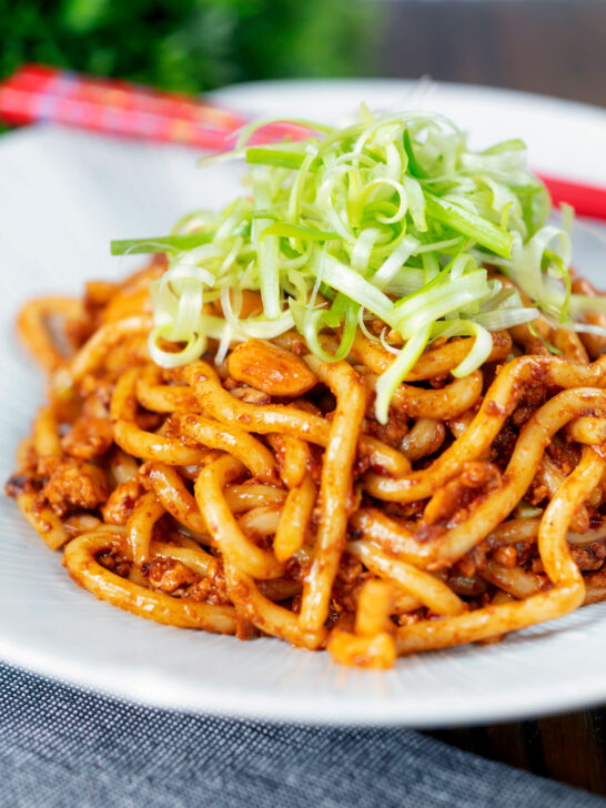 Vegan tofu noodle stir fry with peanuts and dan dan sauce garnished with spring onions.