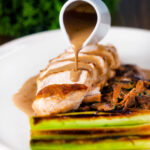 Creamy forestiere sauce poured over a sliced chicken breast served with seared baby leeks.