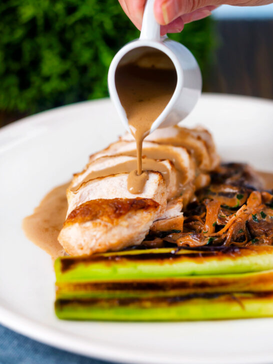Creamy forestiere sauce poured over a sliced chicken breast served with seared baby leeks.
