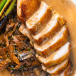 Overhead close-up sliced chicken breast forestiere or mushrooms in a creamy sauce.