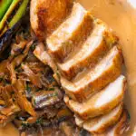 Overhead close-up sliced chicken breast forestiere or mushrooms in a creamy sauce.