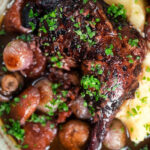 Overhead close up coq au vin, chicken legs braised in red wine with vegetables and bacon.