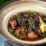 French coq au vin with carrots, mushrooms bacon and shallots served with mashed potato featuring a title overlay.