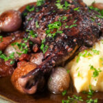 Close up coq au vin, chicken legs braised in red wine with vegetables and bacon.