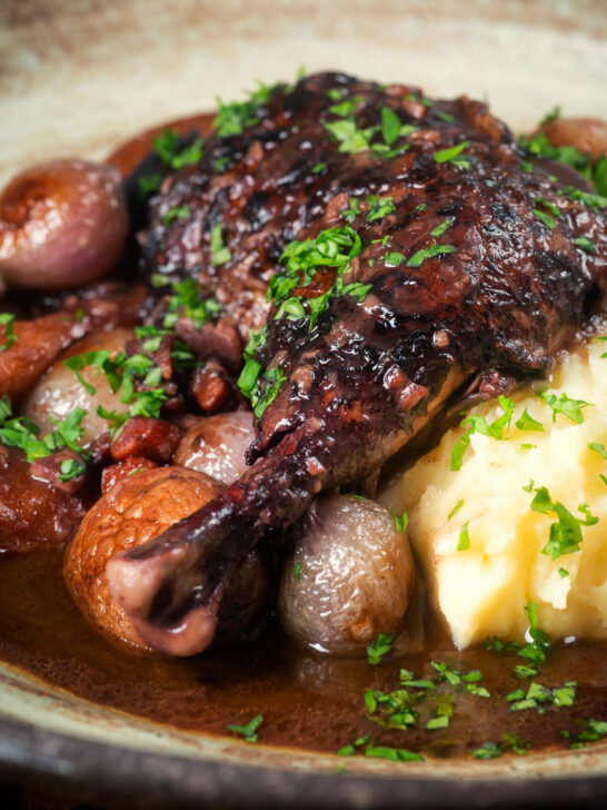 Close up coq au vin, chicken legs braised in red wine with vegetables and bacon.