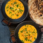 Overhead Indian shahi paneer curry in a creamy sauce served with naan bread.