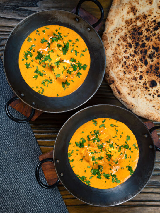 Overhead Indian shahi paneer curry in a creamy sauce served with naan bread.