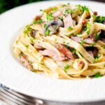 Creamy ham and mushroom tagliatelle with a creme fraiche and mustard sauce featuring a title overlay.