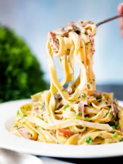 Creamy ham and mushroom tagliatelle with a creme fraiche and mustard sauce on a fork.