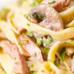 Close-up creamy ham and mushroom pasta with fresh parsley.