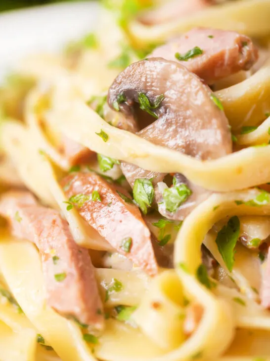 Close-up creamy ham and mushroom pasta with fresh parsley.