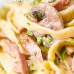 Close up creamy ham and mushroom pasta with fresh parsley featuring a title overlay.