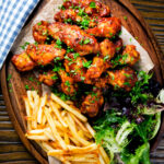Overhead sticky date and harissa chicken wings served with French fries and salad.