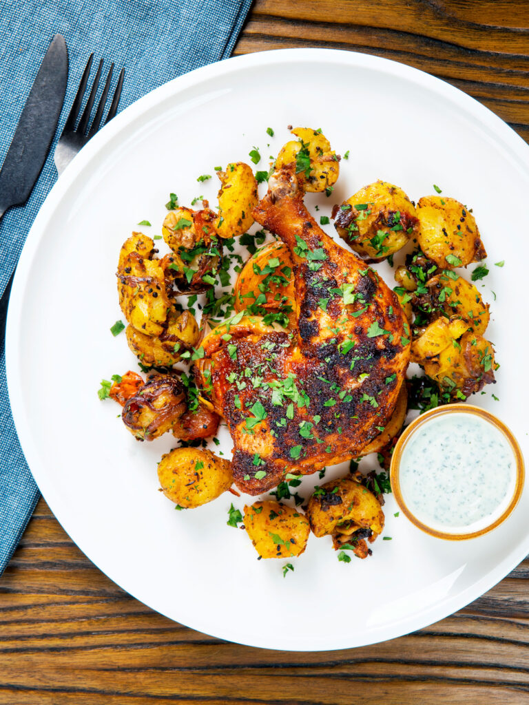 Overhead easy roast chicken legs served with onion and Bombay roast potatoes.