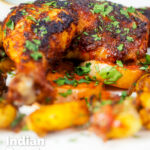 Close-up Indian spiced roast chicken legs served with onion, Bombay potatoes and raita featuring a title overlay.
