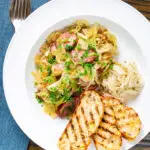 Overhead Polish noodles or lazanki with kielbasa sausage and cabbage served with bread and sauerkraut.