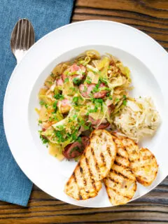 Overhead Polish noodles or lazanki with kielbasa sausage and cabbage served with bread and sauerkraut.