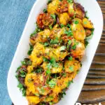 Overhead oven roast Bombay potatoes or Bombay aloo with fresh coriander featuring a title overlay.