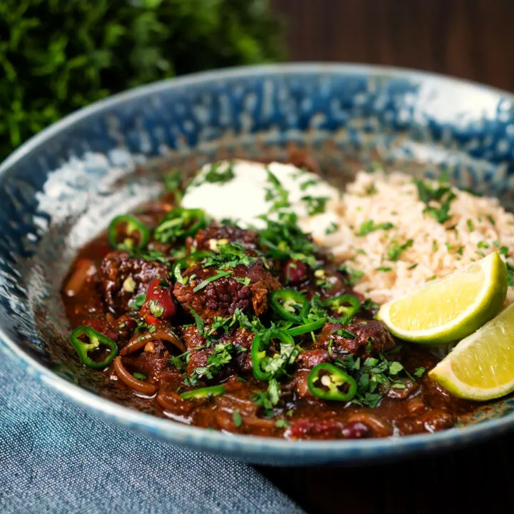 Slow cooker chunky beef chilli con carne with brown rice garnished with lime, coriander and jalapeno.