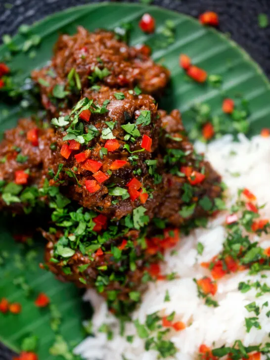 Overhead close-up beef rendang curry with rice, chilli and coriander served on a banana leaf.
