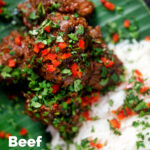 Overhead close-up beef rendang curry with rice, chilli and coriander served on a banana leaf featuring a tittle overlay.