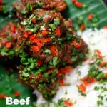 Overhead close-up beef rendang curry with rice, chilli and coriander served on a banana leaf featuring a tittle overlay.