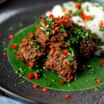 Beef rendang curry with rice, chilli and coriander served on a banana leaf.