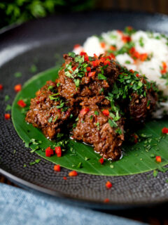 Beef rendang curry with rice, chilli and coriander served on a banana leaf.