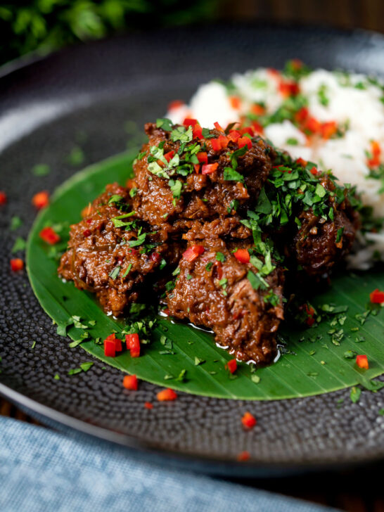 Beef rendang curry with rice, chilli and coriander served on a banana leaf.