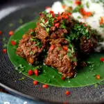 Beef rendang curry with rice, chilli and coriander served on a banana leaf featuring a tittle overlay.