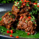 Close-up beef rendang curry with rice, chilli and coriander served on a banana leaf.