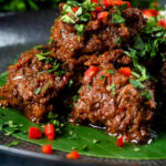 Close-up beef rendang curry with rice, chilli and coriander served on a banana leaf featuring a title overlay.