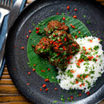 Overhead beef rendang curry with rice, chilli and coriander served on a banana leaf.