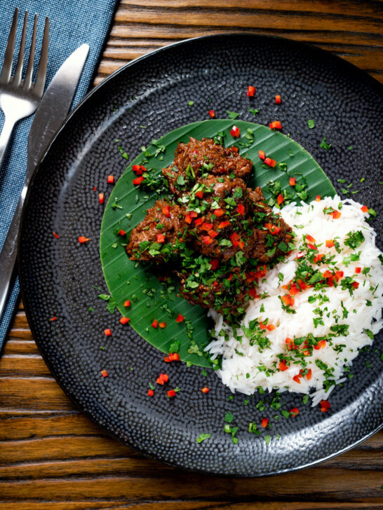 Overhead beef rendang curry with rice, chilli and coriander served on a banana leaf.