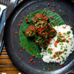 Overhead beef rendang curry with rice, chilli and coriander served on a banana leaf featuring a title overlay.