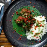 Overhead beef rendang curry with rice, chilli and coriander served on a banana leaf featuring a title overlay.