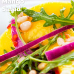 Close-up spicy mango salad with chilli, red onion, rocket (arugula), lime and pine nuts featuring a title overlay.