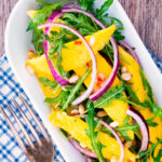 Overhead spicy mango salad with chilli, red onion, rocket (arugula), lime and pine nuts.