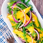 Overhead spicy mango salad with chilli, red onion, rocket (arugula), lime and pine nuts.